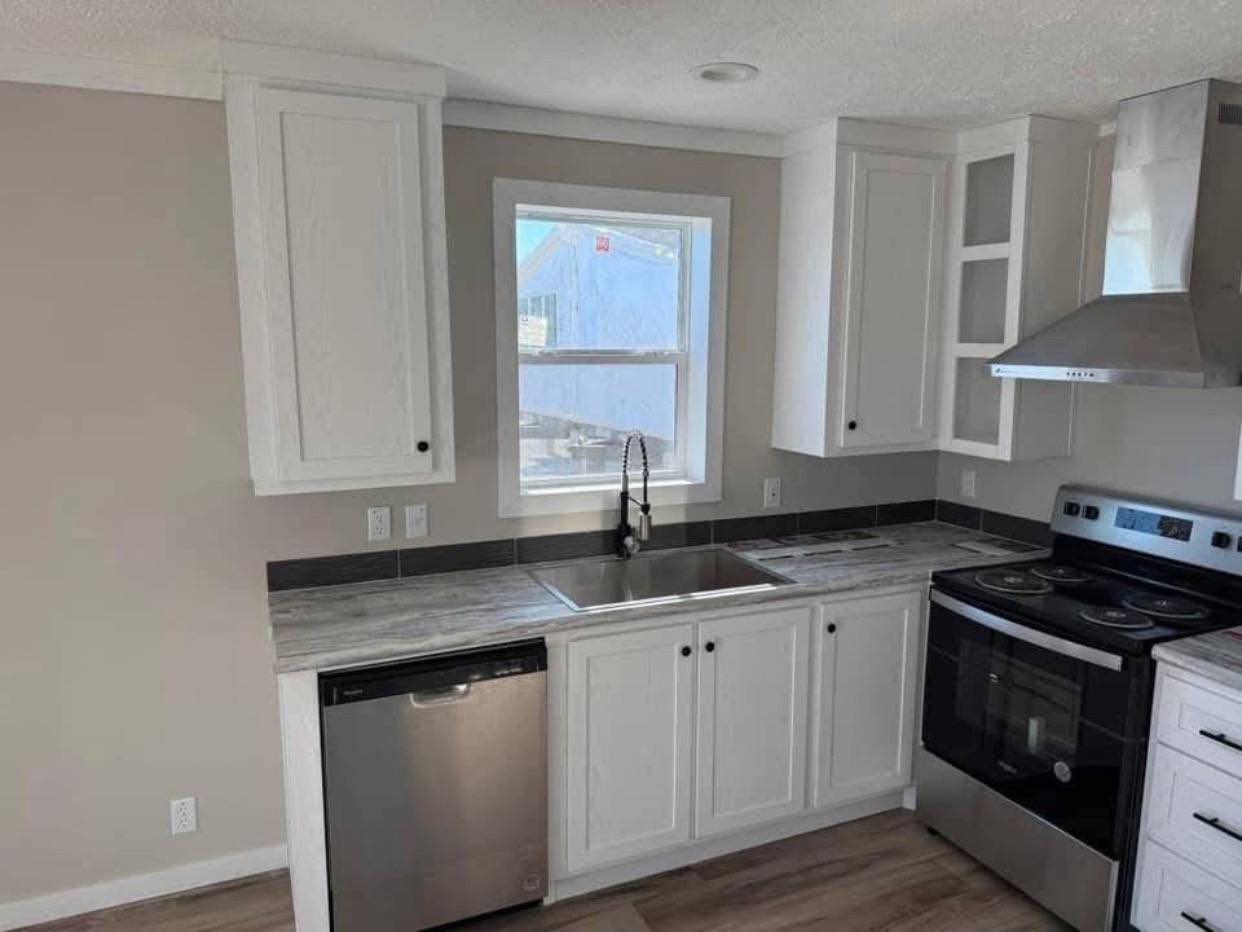 Modern kitchen with white cabinets, stainless steel appliances, and marble countertops. A central window provides natural light, creating a clean, inviting ambiance.
