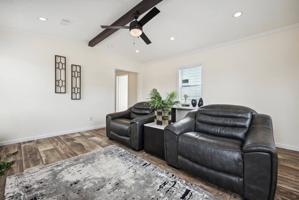 Cozy living room with two dark leather recliners, a modern ceiling fan, indoor plants, and abstract wall art. Natural light creates a warm ambiance.