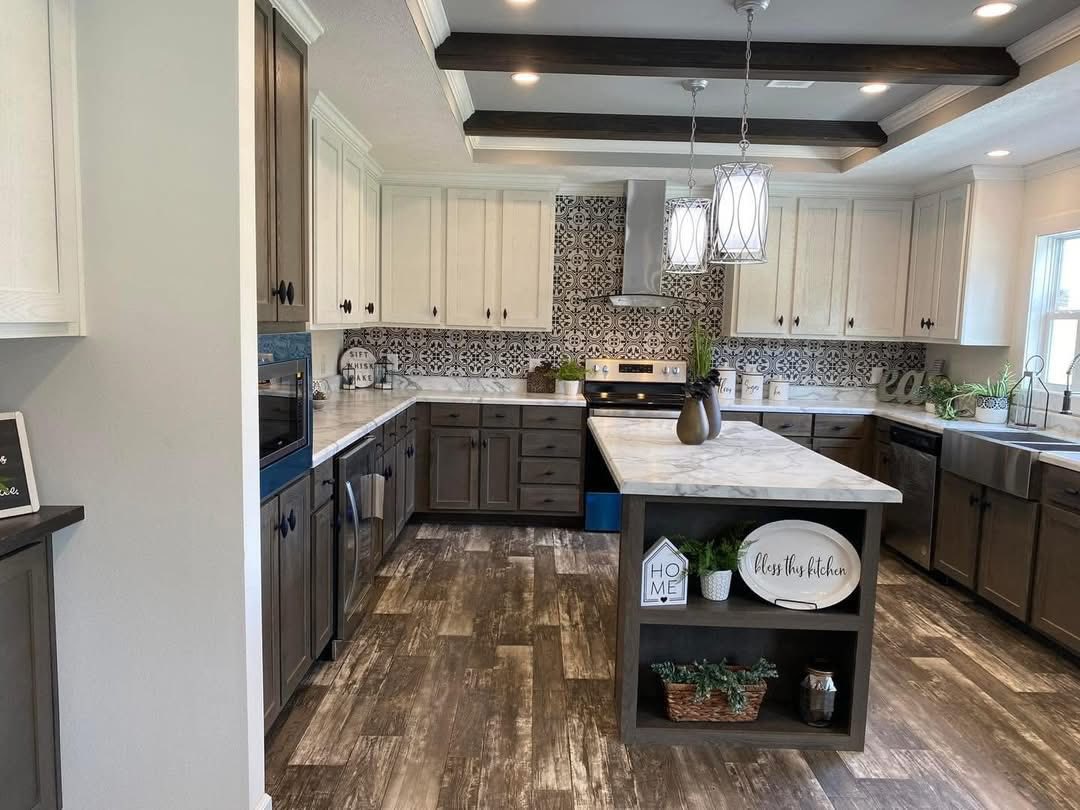 Spacious kitchen with white and gray cabinets, marble countertops, and a patterned backsplash. Warm lighting, decorative signs, and greenery create a cozy atmosphere.