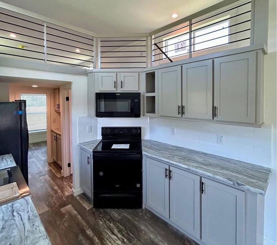 Modern kitchen with gray cabinets, black appliances, and marble countertops. Wood-look flooring and white subway tile backsplash add elegance.