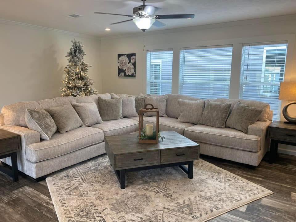 Spacious living room with a light gray sectional sofa, a decorated Christmas tree, and a wooden coffee table on a patterned area rug. Warm, cozy ambiance.