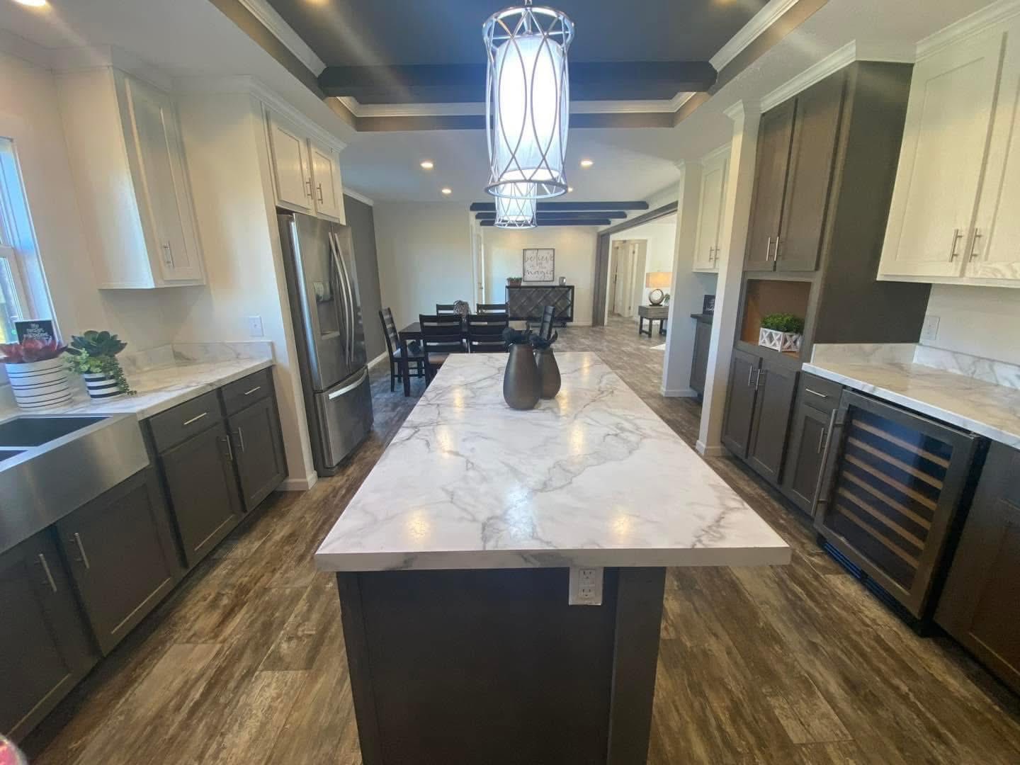 Modern kitchen with a large marble island, pendant light, dark wood cabinets, and hardwood floors. Dining area in the background, well-lit and spacious.