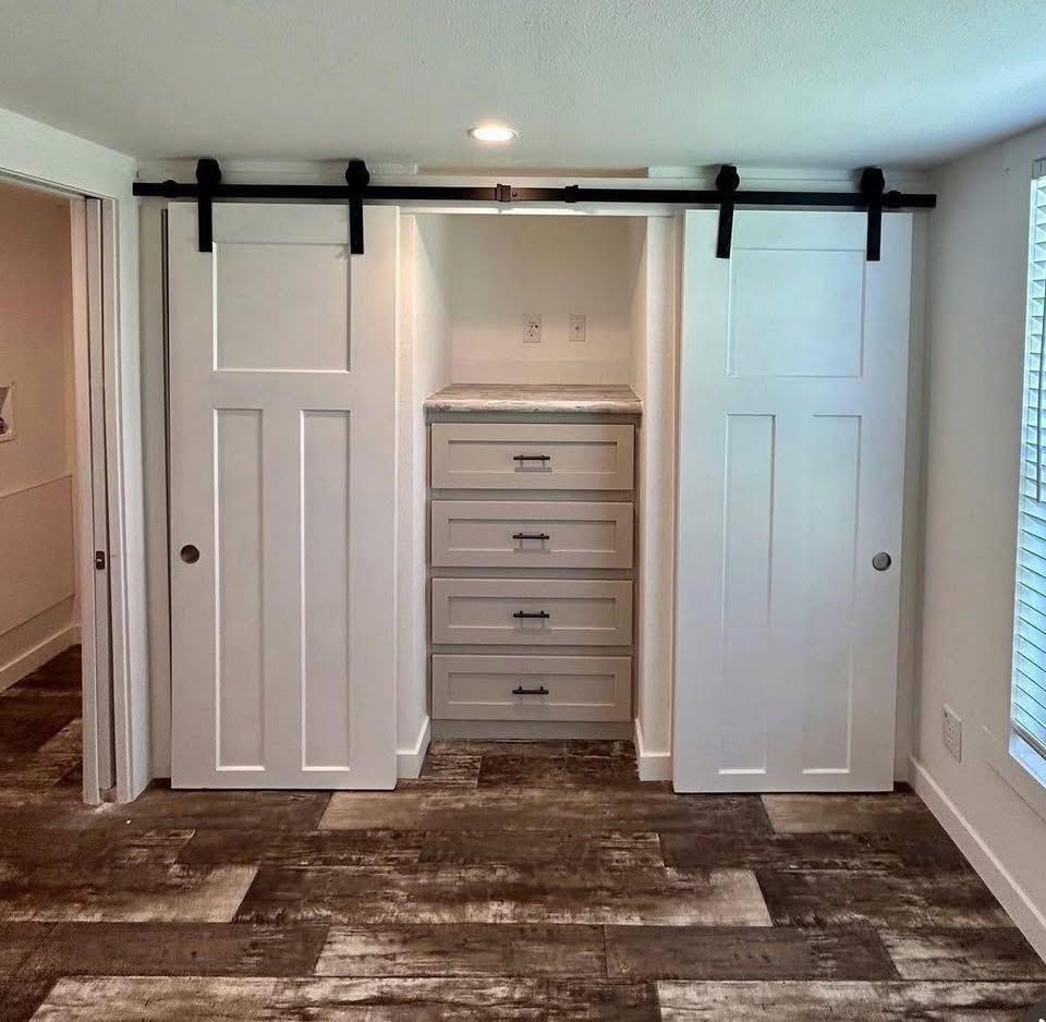 Compact room with white sliding barn doors revealing a built-in dresser and shelves. Warm, rustic flooring creates a cozy, organized atmosphere.