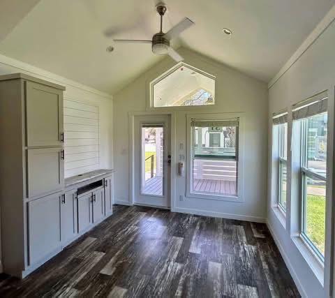 Bright room with vaulted ceiling, wood flooring, and white walls. Contains cabinets on the left, French doors, large windows, and a ceiling fan.