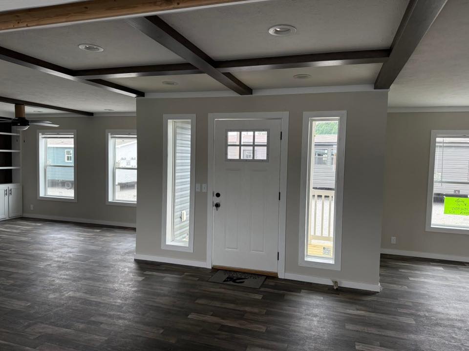Spacious, modern living room with dark wood floors, white walls, and a grid-beamed ceiling. Features a central white door flanked by tall windows.