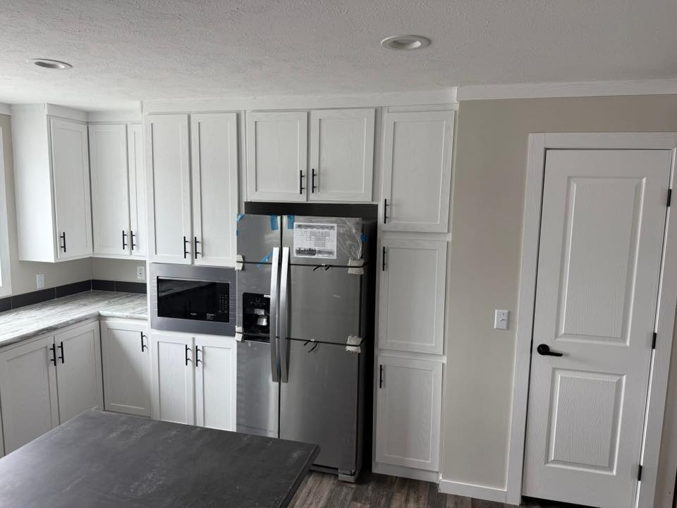 Modern kitchen with white cabinets and black handles, featuring a stainless steel fridge and built-in microwave. Gray countertop surfaces add contrast.
