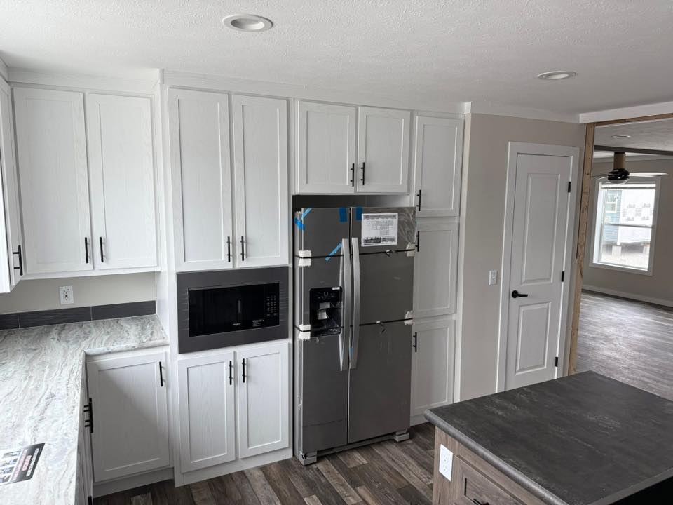 Modern kitchen with white cabinets, stainless steel fridge, and microwave. Gray countertops and wood floor create a sleek, clean look. Bright and airy.