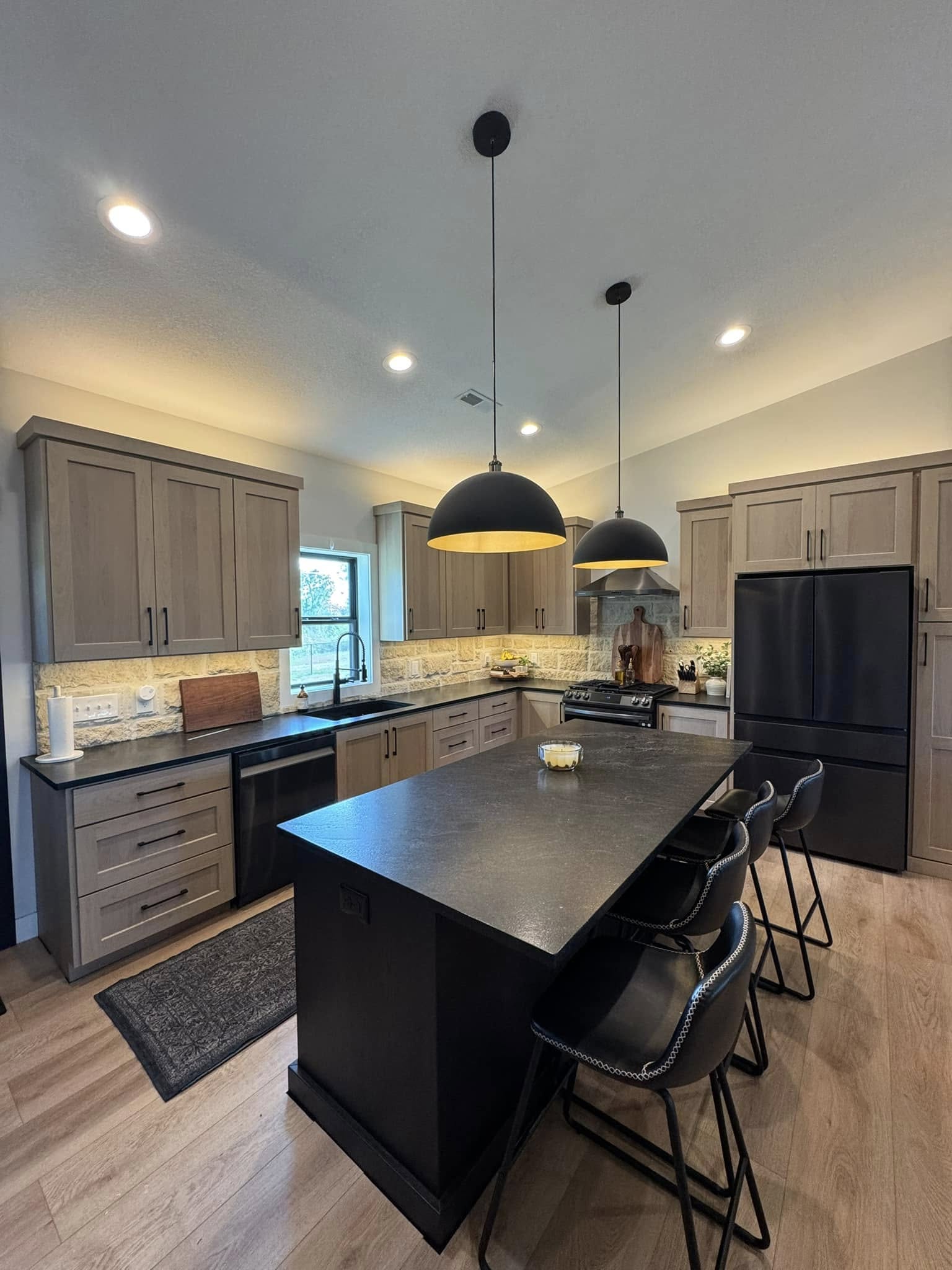 Modern kitchen with sleek wooden cabinets, black countertops, and pendant lights. An island with bar stools is in the center, creating a cozy ambiance.