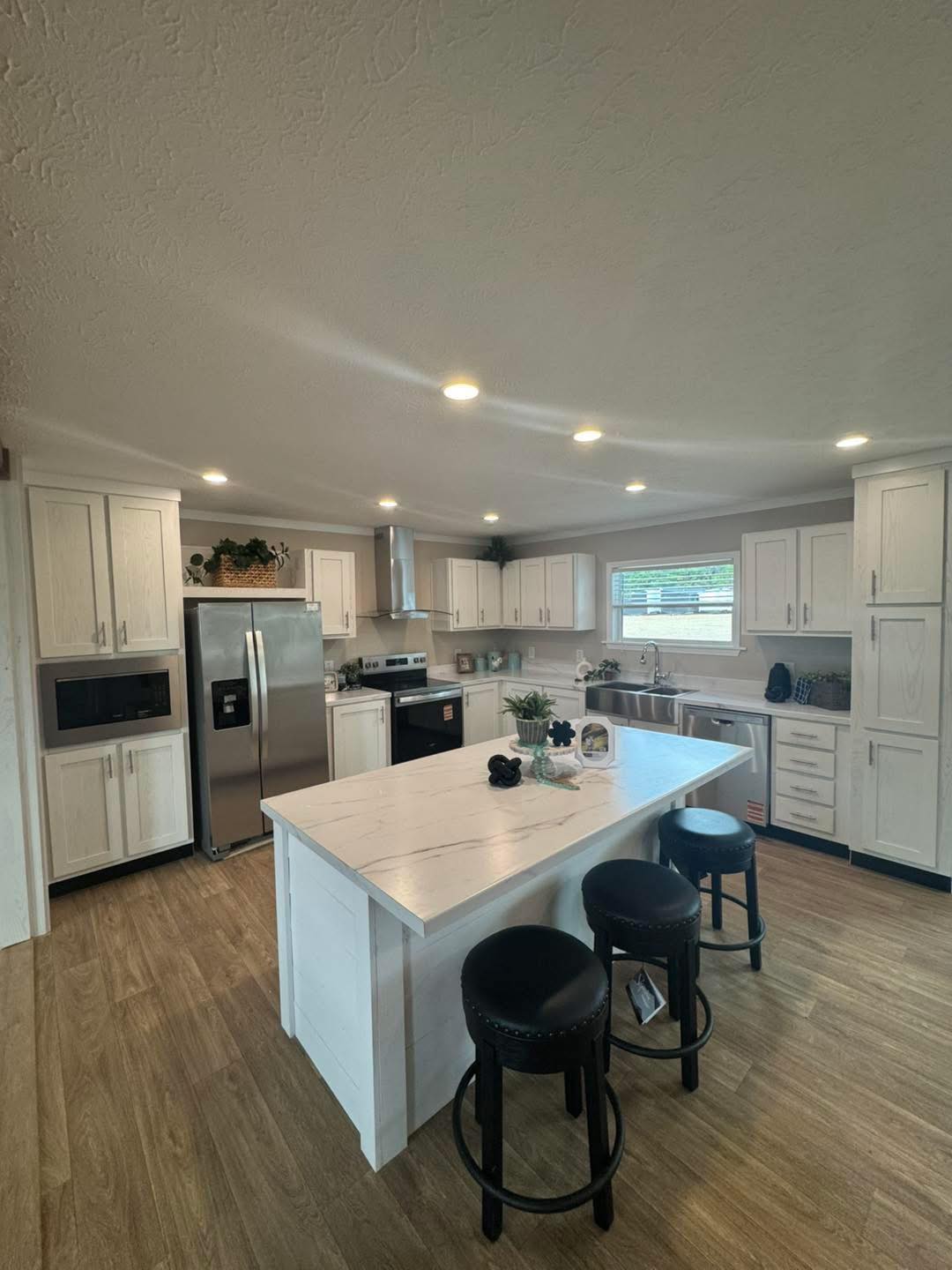 Modern kitchen with white cabinets and island, featuring stainless steel appliances and wooden flooring. Cozy lighting and minimalistic decor enhance the space.