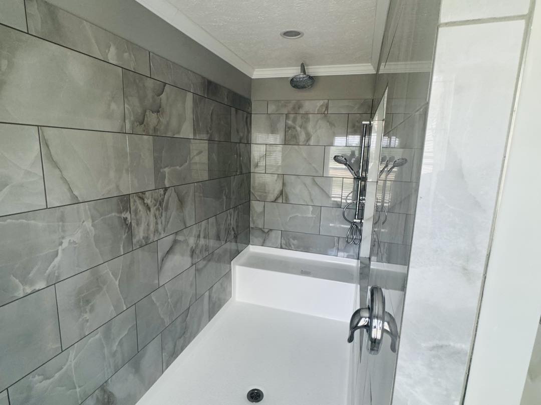 Modern bathroom shower with large gray marble tiles, glass door, and chrome fixtures. It has a bench seat and overhead rain showerhead, conveying elegance.