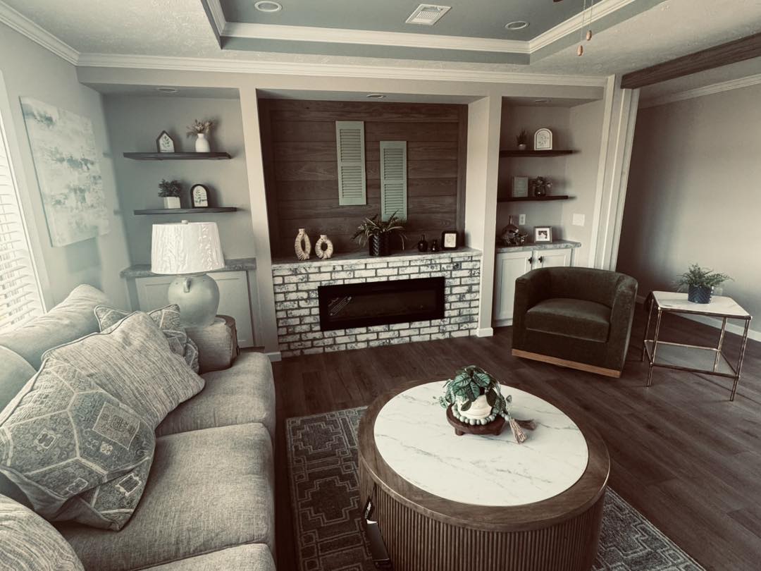 Cozy living room with a gray sofa, marble coffee table, and green armchair. Brick fireplace, shelves with decor, soft lighting create a warm ambiance.