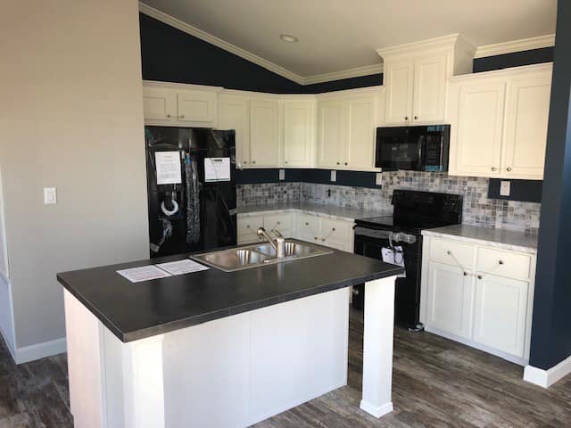 Modern kitchen with dark countertops, white cabinets, and stainless steel sink. Black appliances and mosaic backsplash add contrast. Warm, inviting tone.