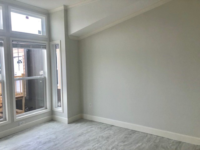 Bright, empty room with light gray walls and a large window on the left, allowing natural light to illuminate the space. Neutral tones create a calm atmosphere.