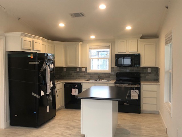 Modern kitchen with white cabinets, black appliances, and a central island. Soft recessed lighting and gray tile backsplash create a sleek, inviting ambiance.