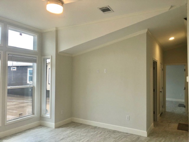 Empty, modern room with high ceilings and beige walls. Large windows let in natural light. A hallway leads to other rooms. Calm, minimalist atmosphere.