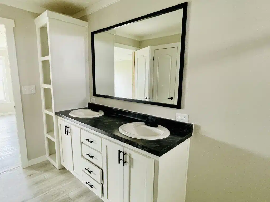Modern bathroom with a double sink vanity. Features black countertop, white cabinets, a large rectangular mirror, and neutral colors for a clean look.