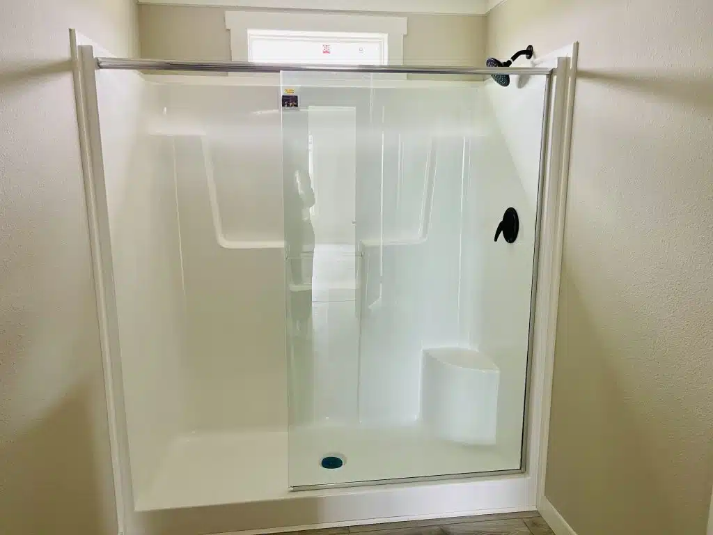 Simple white shower stall with sliding glass doors, black fixtures, and a small built-in seat. Clean, modern design with a soft, natural light.