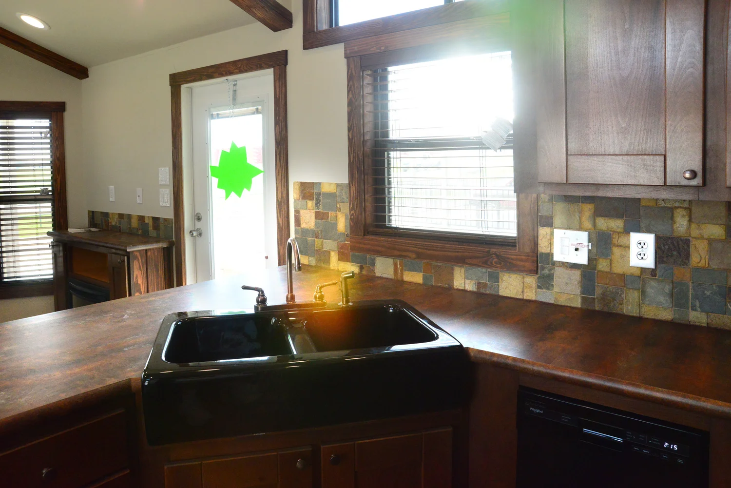 A cozy kitchen with dark wood countertops and cabinetry. A black sink and faucet are centered. Natural light streams through a window, creating a warm and inviting atmosphere.