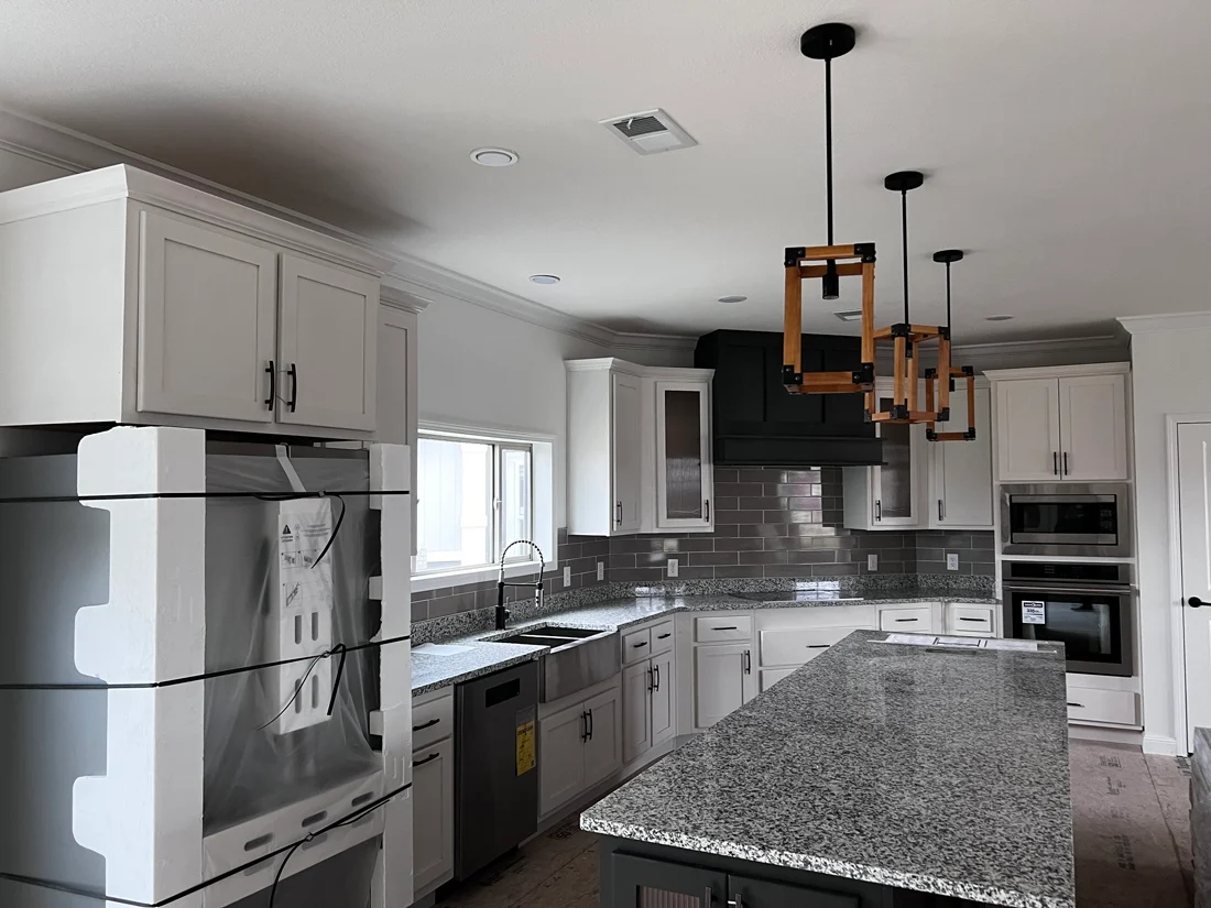 Modern kitchen with white cabinets, granite countertops, and a large island under geometric pendant lights. Stainless steel appliances add a sleek touch.