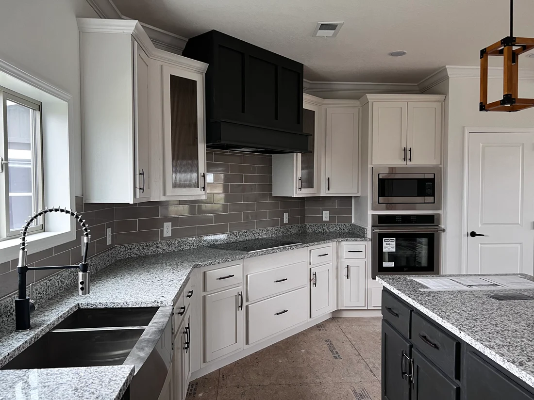 Modern kitchen with white cabinets, gray granite countertops, and stainless steel appliances. Features a large island, tile backsplash, and sleek faucet.