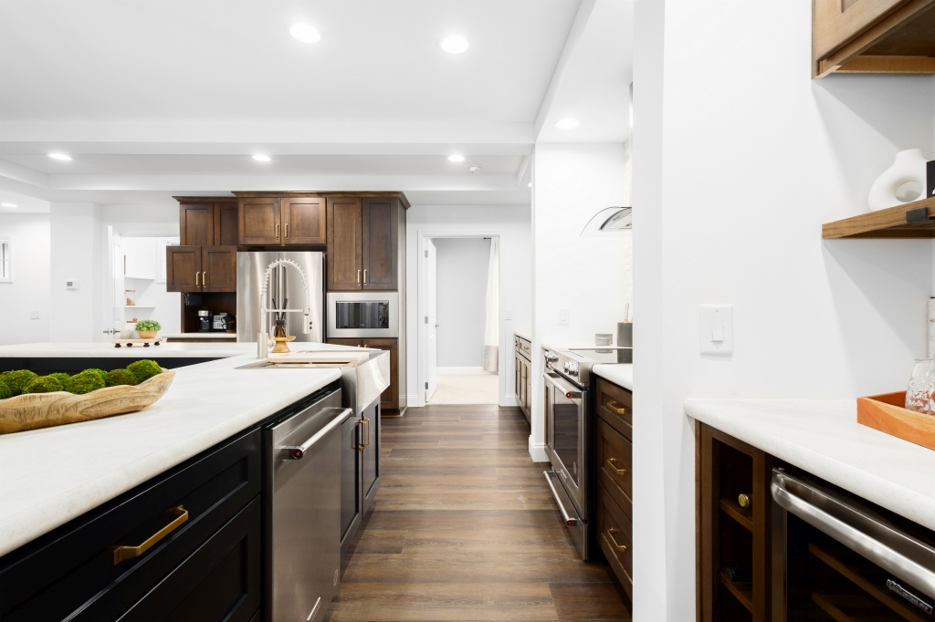 Modern kitchen with dark wood cabinets, stainless steel appliances, and white countertops. Bright lighting and hardwood floors create a warm atmosphere.