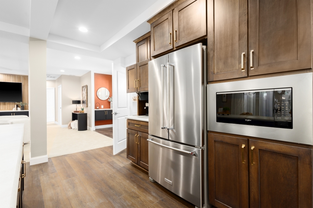 Modern kitchen with warm wooden cabinets, stainless steel refrigerator, and built-in microwave. View opens to a bright living room with sleek decor.