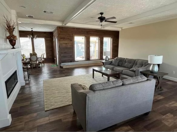 Spacious living room with a gray sectional sofa, wooden floors, and a fireplace. Large windows bring in natural light. Dining area visible in the background.