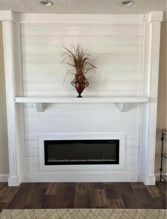 A modern, white shiplap wall features an electric fireplace below a mantel. A decorative vase with tall, dried grass adds elegance. Wooden flooring exudes warmth.