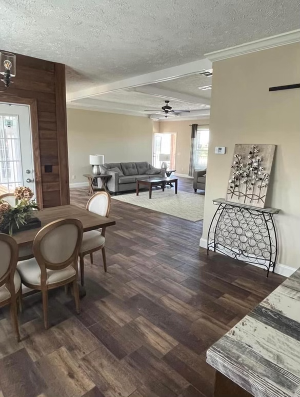 Spacious living area with wooden floors, beige walls, and elegant decor. Includes a dining table with chairs, a gray sofa, and decorative artwork.