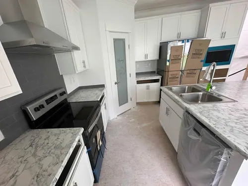 New kitchen with modern appliances, white cabinets, and marble countertops. Boxes and packaging are present, conveying a fresh, clean, and organized space.