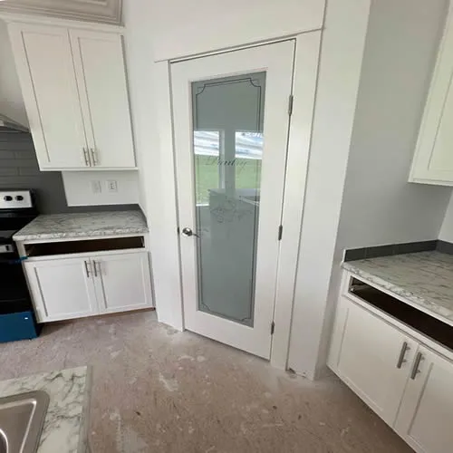 Bright kitchen with white cabinets, marble countertops, and an elegant frosted glass pantry door. Soft, inviting ambiance.