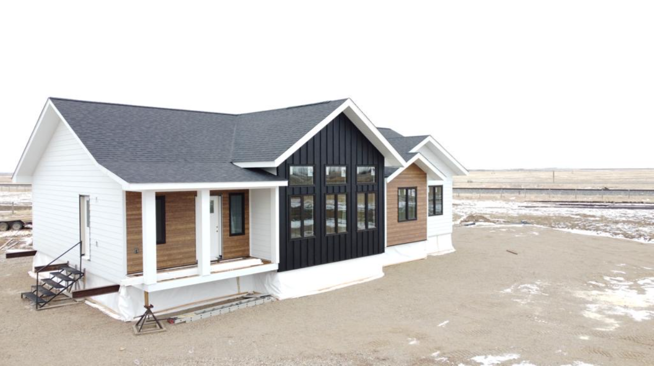 A modern house with contrasting exterior: white and wood siding with a black central section. It sits on a barren, snow-dusted landscape under a pale sky.