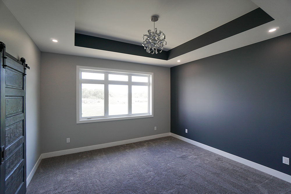 Modern room with gray walls, a white-framed window, and a dark gray accent wall. A chandelier is centered on the recessed ceiling.