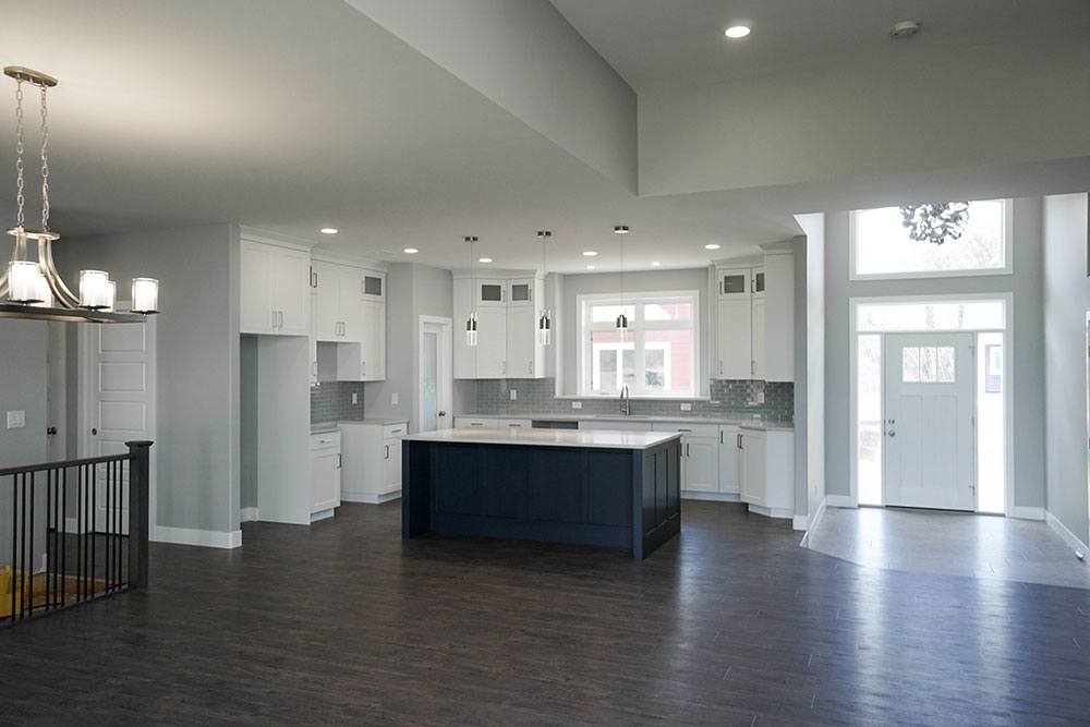 Modern kitchen and dining area with dark wood floors and a navy island. White cabinets and grey backsplash complement the bright, open space.