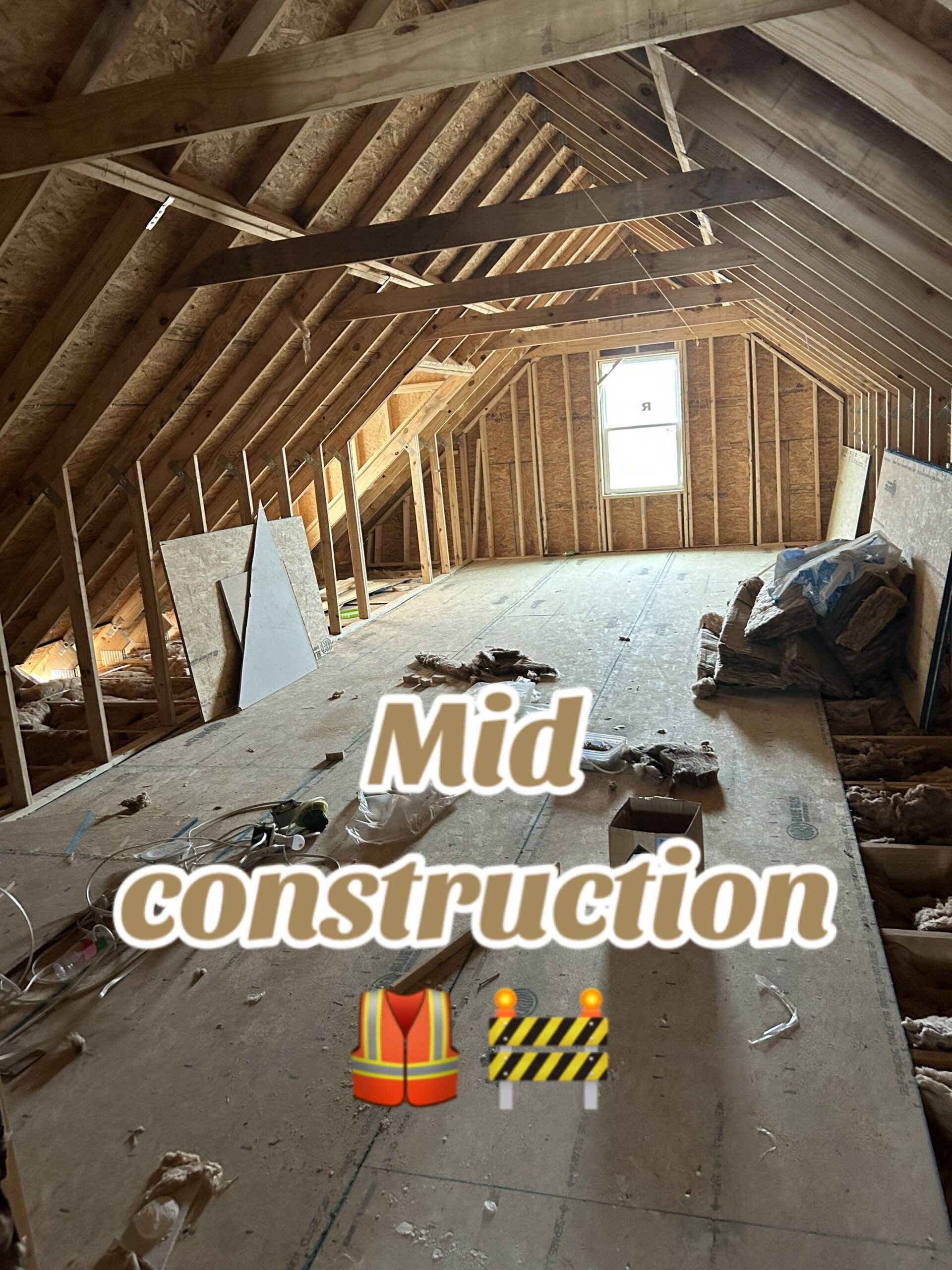 A partially constructed attic room with exposed wooden beams and insulation materials scattered on the floor. Text reads "Mid construction" with construction-themed emojis.