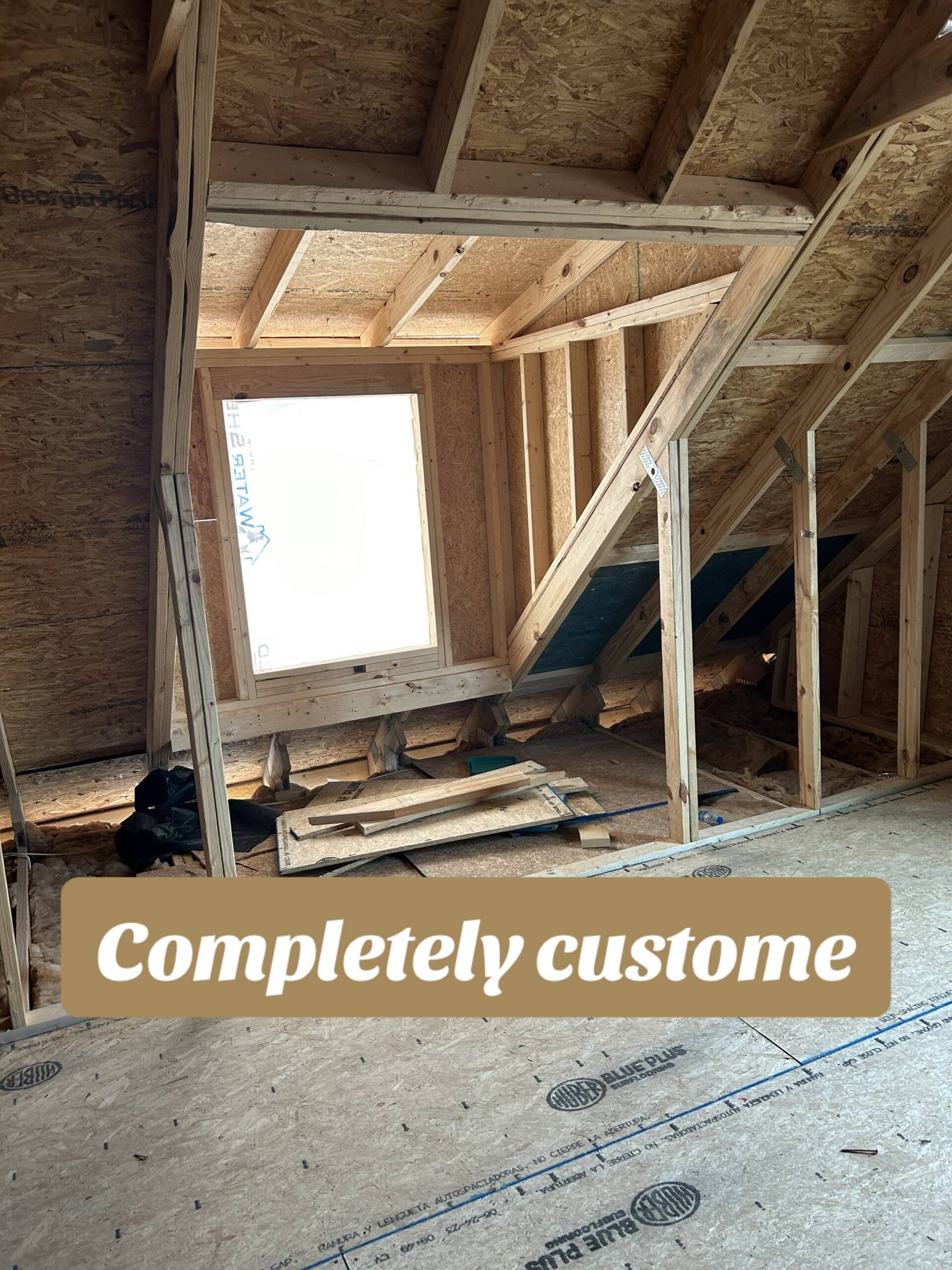 An unfinished attic space with exposed wooden beams and insulation. A large window allows natural light in. Text reads “Completely custom.”