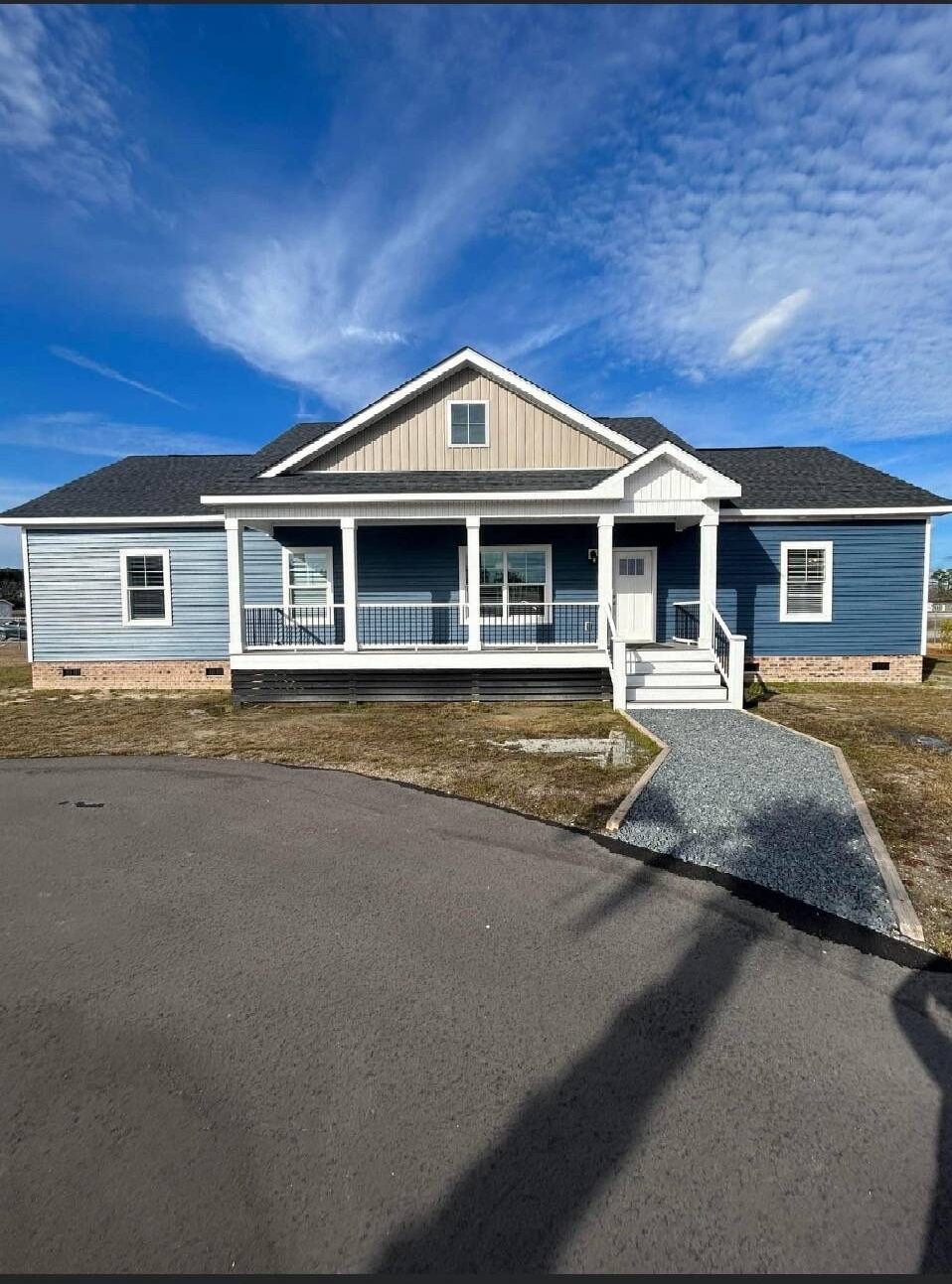 A modern, blue single-story house with white trim, front porch, and a gray roof under a clear blue sky. A walkway leads from the street to the entrance.