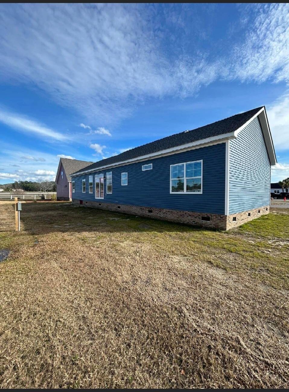A blue, single-story house with white trim sits on a grassy lot under a partly cloudy sky. The scene conveys tranquility and openness.