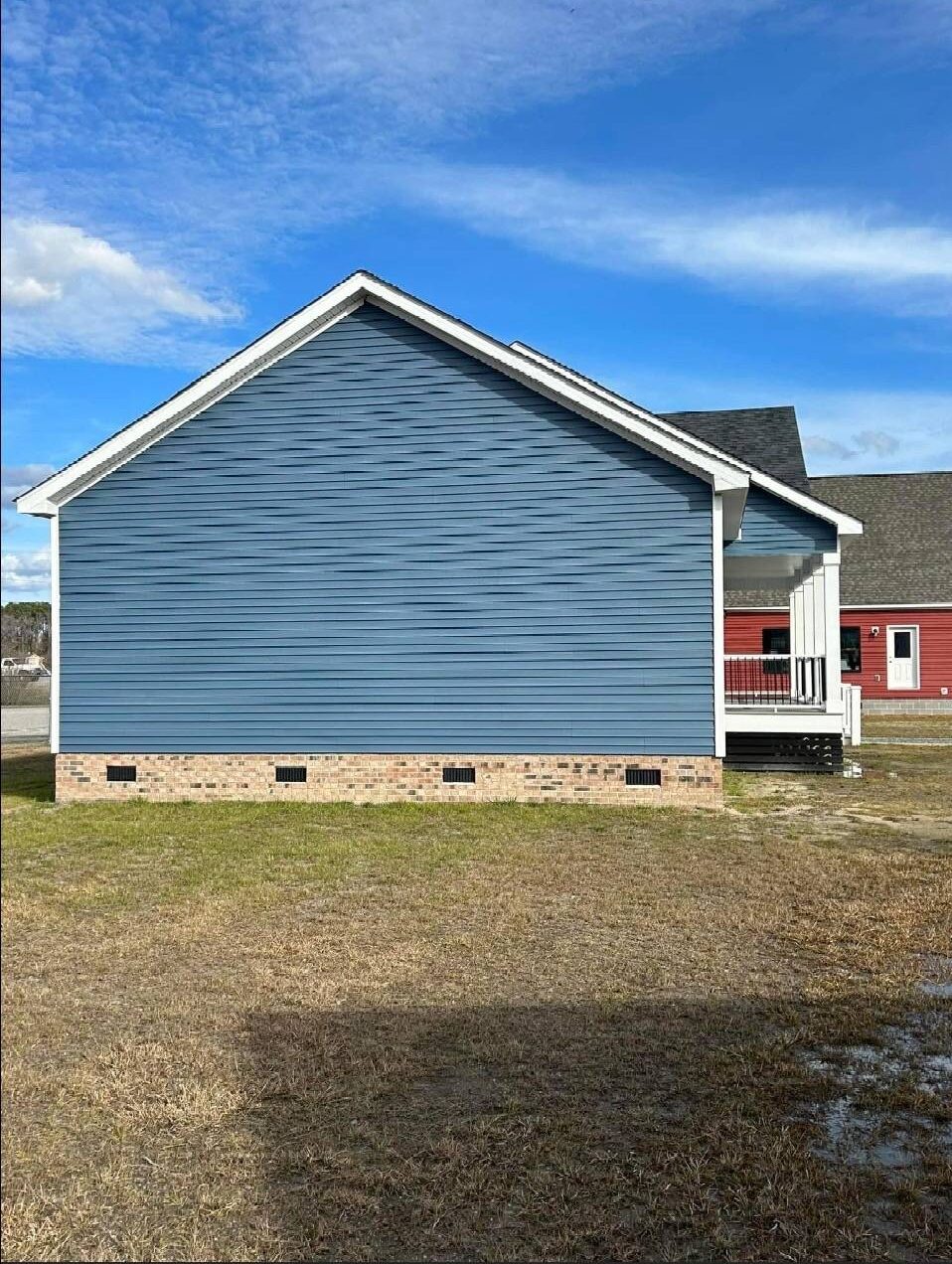 Side view of a blue house with white trim and brick foundation, set against a clear blue sky. A small porch is visible, conveying a calm tone.