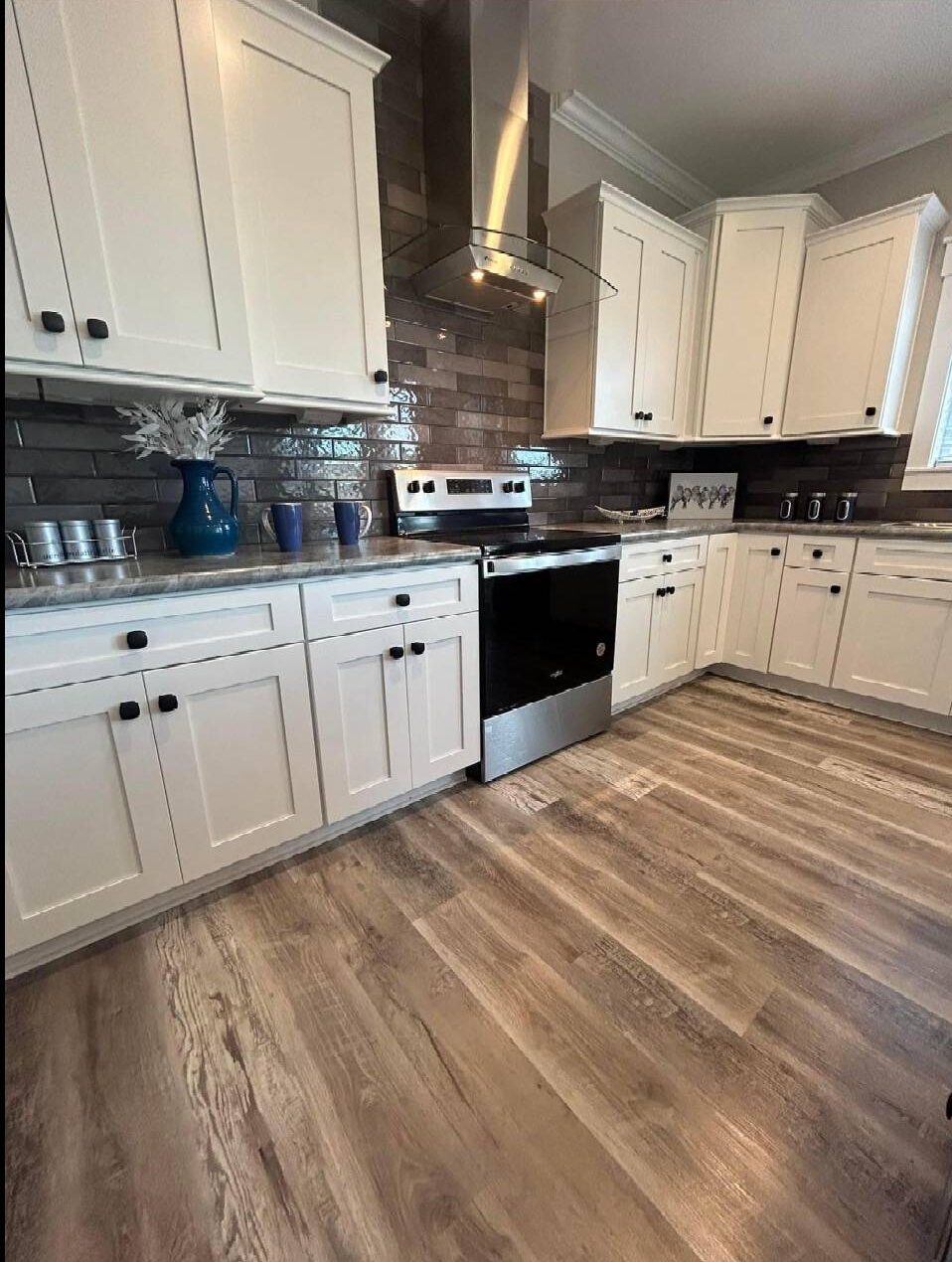 Modern kitchen with white cabinets and black handles, stainless steel appliances, dark brown tile backsplash, and light wood flooring. Cozy and elegant.