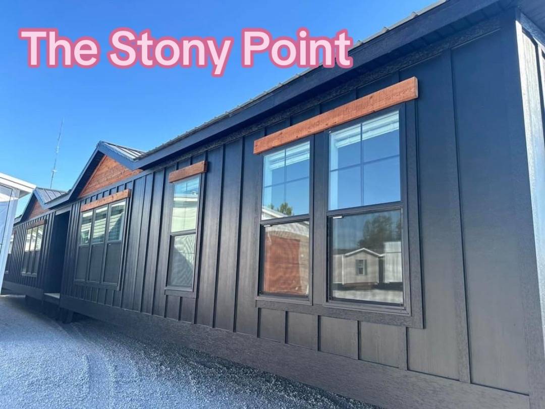 Modern black building with large windows and wooden accents under a clear blue sky, labeled “The Stony Point” in bold pink text.