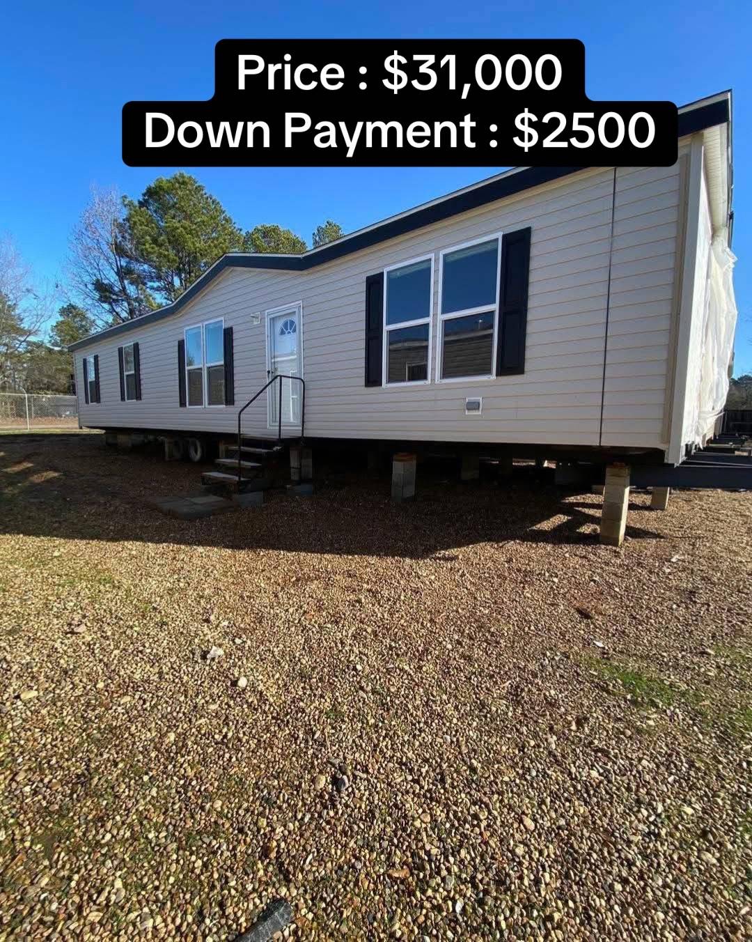 A beige mobile home with black shutters is elevated on concrete piers in a gravel yard. A text overlay reads "Price: $31,000, Down Payment: $2,500."