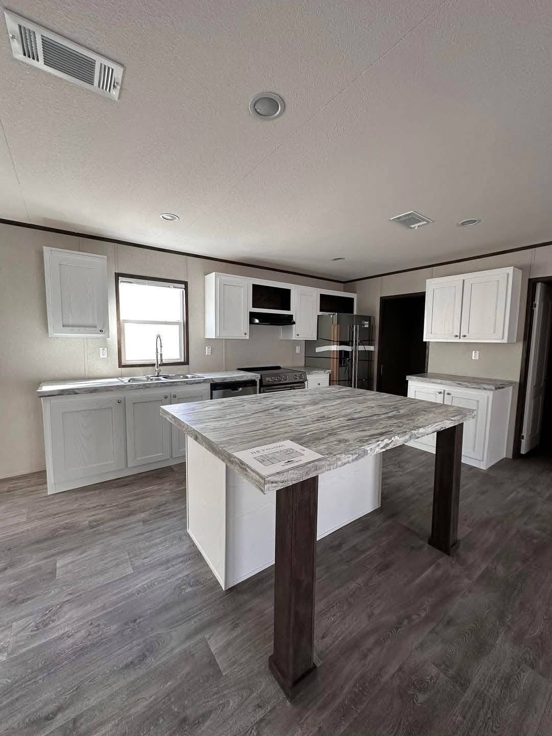 Spacious kitchen with a central marble island, gray flooring, and white cabinetry. Features include stainless steel appliances and a modern, minimalist design.