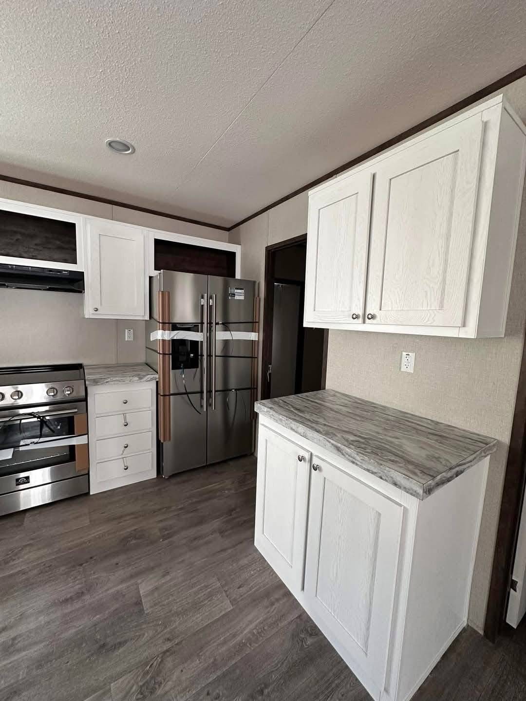 A modern kitchen with white cabinets and marble countertops. Stainless steel appliances include a refrigerator and stove. The room has light wood flooring.