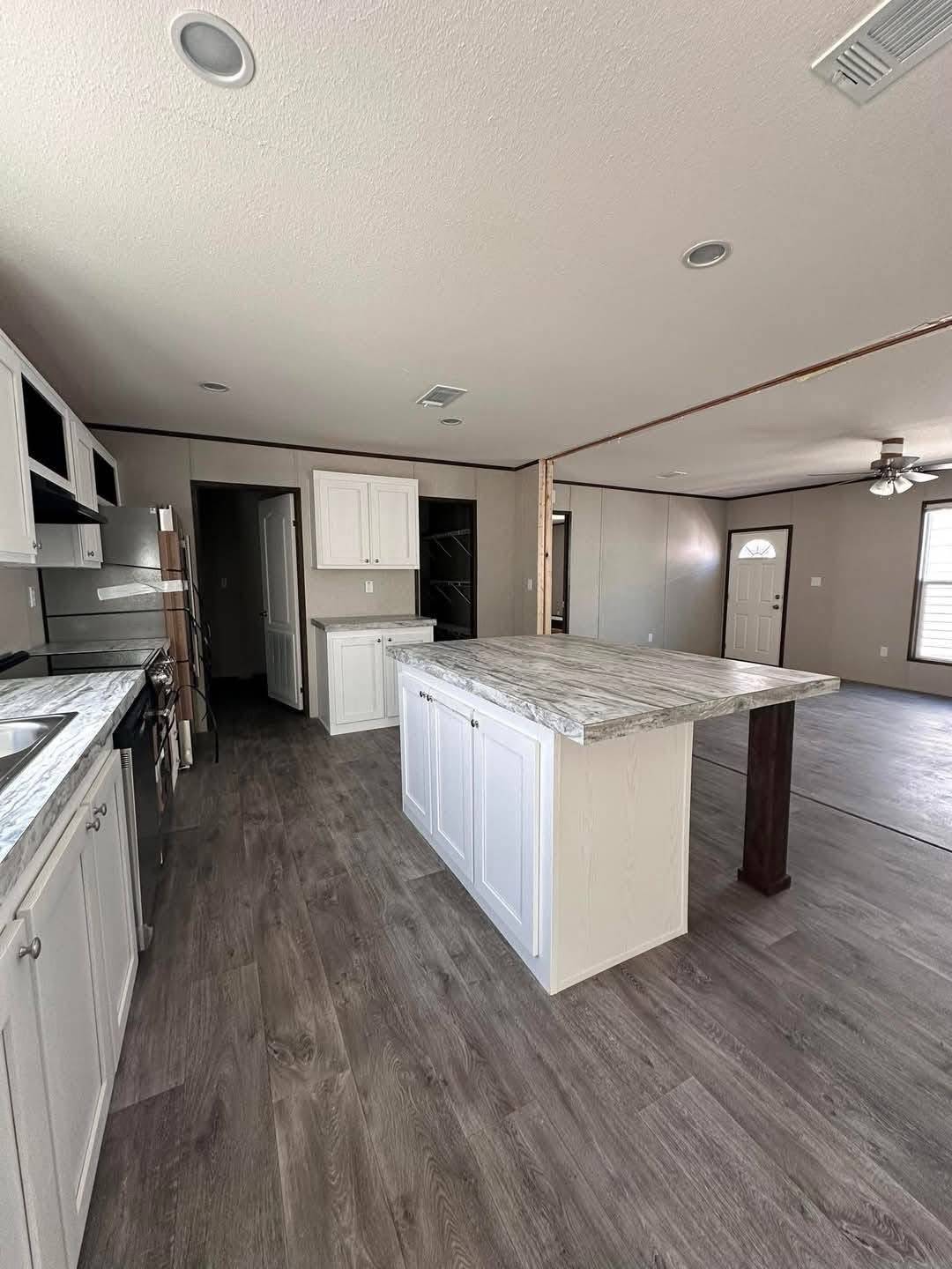 Spacious kitchen and living area with white cabinets, marble countertop island, and wood laminate flooring. Light and airy with modern fixtures.