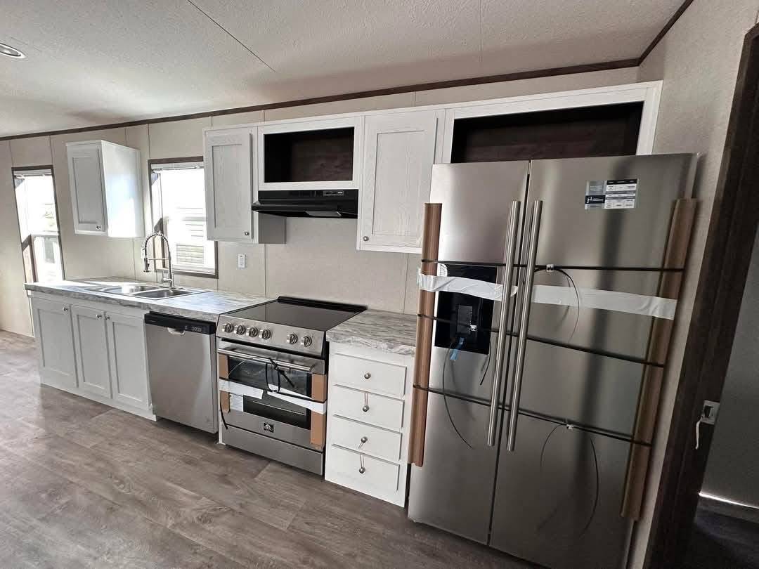 Modern kitchen with stainless steel appliances, including a double-door fridge and oven. White cabinets, marble countertop, and a sleek, clean design.