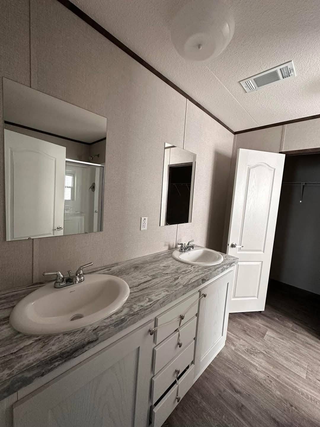 Modern bathroom with dual sinks and marble countertop. Two mirrors hang above the sinks. An open white door reveals a closet. Neutral tones create a calm atmosphere.