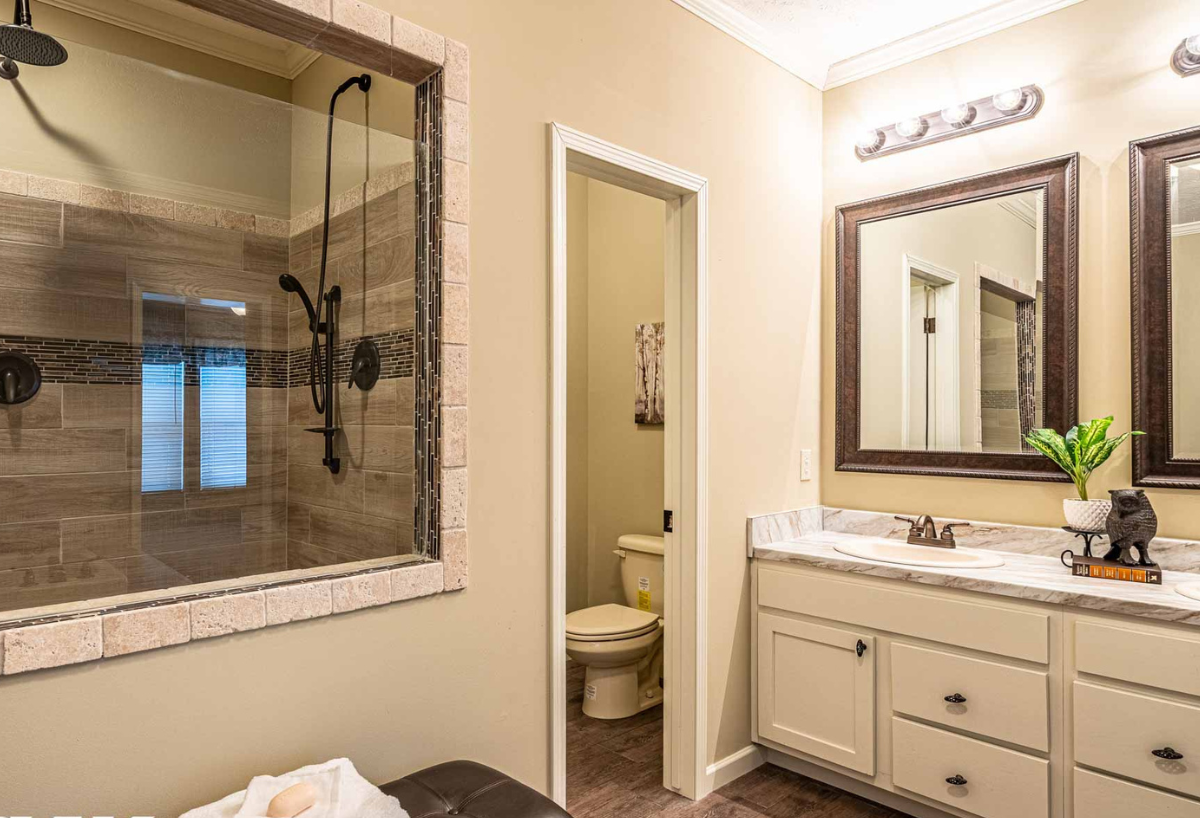 Modern bathroom with a large glass shower on the left, featuring brown tiles. A vanity with dual sinks and mirrors is on the right, exuding a cozy, elegant feel.