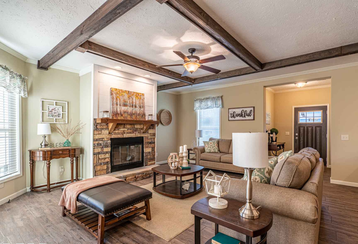 Cozy living room with beige walls and wood accents. Features a stone fireplace, sofas, and a ceiling fan, creating a warm and inviting atmosphere.