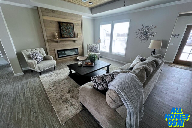 Living room with cozy beige sofas, patterned accent chairs, and a dark wood coffee table on a light rug. Wooden fireplace, large windows, and neutral tones create a warm, inviting atmosphere. Image for illustrative purposes.